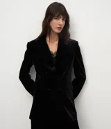 Blazer de terciopelo color negro con largo extendido, diseño cruzado con botones frontales, solapa clásica, bolsillos con tapa y mangas largas.