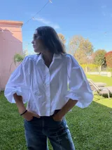 Camisa de color marrón oscuro con cuello clásico y mangas abullonadas con puños elásticos. Presenta un corte holgado y cierre frontal con botones.