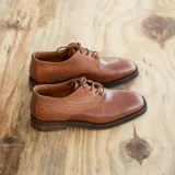 Zapato mocasín de cuero vacuno color negro, con cordones y punta redonda. Tiene taco de madera foliado en cuero de 2,5 cm y entre suela de goma de 1 cm.