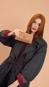 Billetera larga de símil cuero color marrón claro, con solapa frontal decorada con un aro metálico central. Cuenta con múltiples compartimentos internos para tarjetas, billetes y un monedero con cierre.