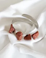 Brazalete rígido plateado con cuatro piedras del sol sintéticas engarzadas.
