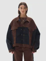 Campera tipo trucker oversize con diseño colorblock en tonos marrón y negro. Confeccionada en tejido de algodón, presenta costuras a la vista en contraste, bolsillos frontales con solapa y cierre mediante botones metálicos.