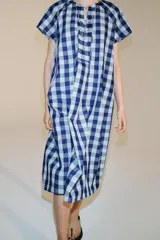 Vestido midi de Zara Woman Collection confeccionado en mezcla de viscosa, con estampado de cuadros en tonos azul y celeste. Presenta cuello redondo, manga corta, bolsillos ocultos en las costuras y cierre frontal con cordones entrelazados.