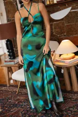 Vestido largo de satén con estampado abstracto en tonos verdes y azules, con escote halter cruzado, detalle de frunce en el pecho y tajo lateral profundo.