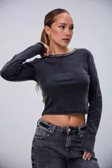 Remera negra de manga larga con efecto acid wash y cuello redondo decorado con tachas plateadas.