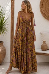 Vestido largo en tono mostaza con estampado paisley y floral en tonos morados y oscuros, escote en V profundo con tiras ajustables con borlas y tirantes finos en los hombros con cordones decorativos colgantes.