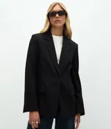 Blazer de sastrería confeccionado en tejido de poliéster con acabado liso. Presenta un diseño de corte regular con solapas clásicas, cierre frontal de un botón y mangas largas con botones forrados en los puños. Incluye bolsillos con solapa y forro interior.