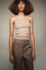 Pantalón marrón de tiro alto con bolsillos delanteros y traseros. El bajo está acabado con vuelta. Cierre frontal con cremallera y ganchos metálicos.