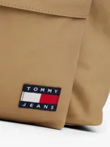 Mochila de diseño redondeado color beige, con compartimento principal y bolsillo frontal con cierre. Incluye parche con logo de la marca en la parte inferior, asa superior y correas acolchadas ajustables.