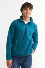 Buzo de polar color azul petróleo, con cuello alto y cierre frontal parcial. Cuenta con bolsillos laterales y mangas largas.