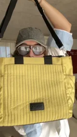 Cartera tipo tote de nylon color malva, con diseño capitoneado de líneas verticales en el frente y rombos en los laterales. Cuenta con doble asa de mano en color negro, bolsillos laterales y un parche decorativo con logo en la parte frontal.