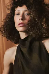 Top de cuello halter con espalda descubierta, confeccionado en tejido de viscosa con estampado de cuadros en tonos verde oliva y negro. Presenta un diseño asimétrico en el bajo y cierre con botones en la parte posterior del cuello.
