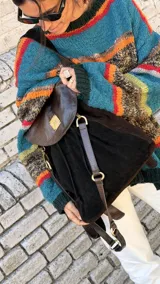 Mochila Brassy confeccionada en combinación de gamuza marrón oscuro y cuero negro, con solapa de cuero texturado y herrajes metálicos en tono oro viejo. Presenta correas regulables y diseño funcional para el día a día.