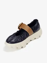 Zapato de cuero azul marino con correa marrón con hebilla dorada y suela de goma blanca con diseño ondulado.