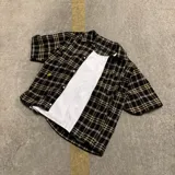 Camisa de manga corta con corte boxy fit, diseño a cuadros en tonos marrones, amarillos y azules, con cierre frontal de botones y bolsillo en el pecho.