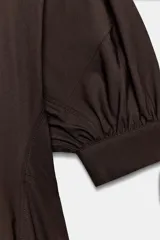 Vestido midi de algodón con cuello solapa, cierre frontal con botones y mangas cortas abullonadas con puños. Presenta un diseño evasé con bolsillos laterales ocultos y elástico en la espalda.