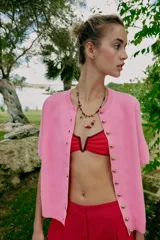 Chaqueta de punto de manga corta en color rosado, con cuello redondo y cierre frontal de botones dorados.