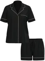 Pijama corto de modal negro compuesto por una camisa de manga corta con botones, bolsillo en el pecho y cuello solapa, y un short a juego con cintura elástica y cordón ajustable. Ambas piezas cuentan con ribetes blancos en contraste.