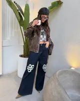 Pantalon de jean azul oscuro de corte ancho y tiro medio, con costuras a la vista en color contrastante y estampado gráfico de logo en blanco sobre ambas rodillas.