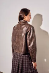 Campera de cuero vegano en tono marrón con acabado desgastado, corte recto y cierre frontal con botones a presión. Presenta cuello clásico y diseño minimalista.