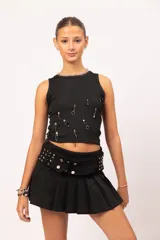 Musculosa negra de cuello redondo y calce entallado, decorada con alfileres de gancho plateados, cuentas negras y dijes metálicos dispuestos de forma irregular en el frente.