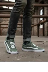 Championes urbanos de estilo skate, color verde oliva, con cordones blancos y suela de goma blanca con detalle de línea negra. Presentan un diseño lateral característico con una franja blanca en forma de V.