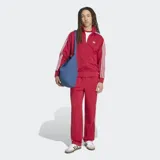 Pantalón deportivo Adidas Firebird Drop Needle de color rojo con rayas verticales finas, bolsillos laterales con cierre y las icónicas tres tiras blancas a lo largo de los laterales. Incluye el logo del trifolio bordado en la pierna.