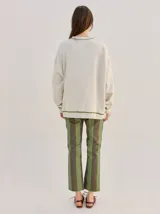 Buzo oversize color gris melange con corte crew, cuello redondo, mangas largas y detalles bordados en color verde en el cuello, puños y ruedo. Presenta el logo de la marca bordado en el pecho.