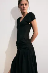 Vestido midi color negro de escote en V y manga corta, con detalle de fajín drapeado cruzado en la cintura y falda abullonada de corte asimétrico.