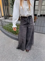 Pantalón de jean estilo wide leg en color gris oscuro con efecto lavado. Presenta un corte de tiro alto, costuras verticales marcadas en el frente y una silueta amplia y fluida.