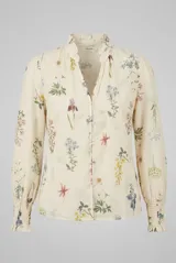 Camisa de manga larga color arena con delicado estampado botánico de flores silvestres. Presenta cuello alto con volados, escote en V con cierre frontal de botones y puños ajustados con nido de abeja.