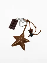 Llavero de metal con múltiples dijes colgantes: una barra de chocolate, una estrella de cuero marrón con tachas doradas, un mosquetón en forma de corazón y cordones de gamuza con cuentas decorativas.
