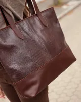 Bolso tipo tote de cuero vacuno color chocolate, con textura efecto cocodrilo en la parte superior y base lisa. Cuenta con doble asa de hombro y cierre superior.