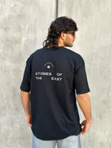 Remera negra de corte oversize con estampado en la espalda que dice 'REAL ADVENTURE STORIES OF THE EAST'.