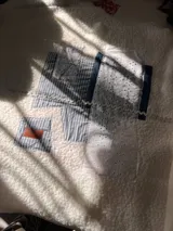 Campera de estilo patchwork confeccionada en tejido tipo corderito blanco, con parches de tela de algodón a rayas azules y blancas, encaje bordado blanco y detalles en denim. Presenta una etiqueta de cuero sintético con el logo de la marca.