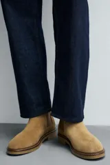 Bota estilo Chelsea de hombre, color marrón, fabricada en piel con acabado serraje (gamuza). Presenta elásticos laterales oscuros y suela de goma a tono con tacón bajo.