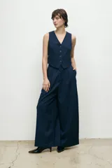 Pantalón sastre de corte wide leg y tiro alto, en color beige. Presenta pinzas frontales, cierre con botón y bolsillos laterales.