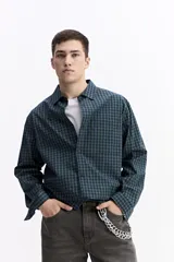 Camisa de popelina a cuadros, color celeste y blanco, de manga larga y corte holgado. Presenta un bolsillo frontal y cartera abotonada.