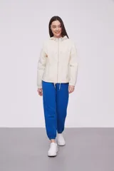 Campera liviana color crema con capucha, cierre frontal completo y cordones ajustables en el cuello y el ruedo. Cuenta con mangas largas con puños elásticos y bolsillos laterales.