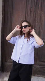 Camisa de corte boxy fit color celeste, con mangas cortas y cuello tipo polo. Presenta un estampado frontal en color rojo con la frase 'CALL MY STYLIST' y un detalle bordado en color negro con la firma 'FACHAPOSTA'.