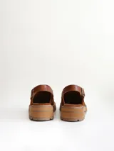 Zueco de cuero gamuzado color óxido, con tira trasera ajustable mediante hebilla metálica. Presenta una suela de plataforma con textura acanalada y detalle de textura reptil en la tira posterior.