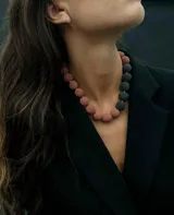Collar de piedras volcánicas naturales con diseño de esferas texturizadas en tonos rosado y gris oscuro, dispuestas de forma asimétrica.