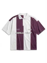 Chomba de piqué con diseño color block vertical en negro y verde oscuro, cuello polo y cierre frontal parcial. Presenta inscripciones en el frente.