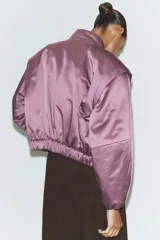 Chaqueta acolchada de cuello subido con cierre frontal de cremallera, manga larga con hombros marcados y puños elásticos. Presenta un diseño con bajo elástico y acabado satinado.