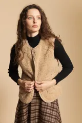 Chaleco de textura tipo corderito en color beige, con cierre frontal de botones a presión y bordes ribeteados. Presenta un diseño sin mangas con silueta relajada.