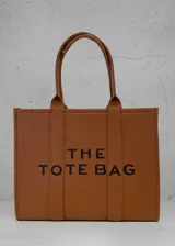 Cartera tipo tote bag color tostado con diseño estructurado, doble asa superior y estampado frontal con la leyenda 'THE TOTE BAG' en color negro.