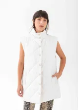 Chaleco acolchado de corte largo, con cuello alto y cierre frontal mediante botones a presión. Presenta un diseño de rombos pespunteados y bolsillos laterales.