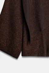 Jersey de punto marrón oscuro con hilo metalizado, cuello bote y manga ancha. Presenta un diseño asimétrico en la parte delantera con una capa superpuesta diagonal.