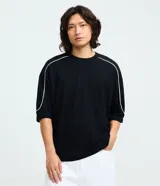 Remera de algodón color negro, con cuello redondo, manga corta y detalle de raya blanca contrastante que recorre la línea del hombro y la manga. Presenta un corte holgado y cómodo.