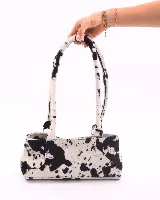 Cartera tipo baguette confeccionada en cuero vacuno con pelo y estampado animal print de vaca. Presenta doble asa de hombro, cierre superior y broches laterales para ajustar su volumen.
